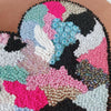 Close-up of a colorful beaded and embroidered abstract heart artwork on canvas with varied textures and shades.