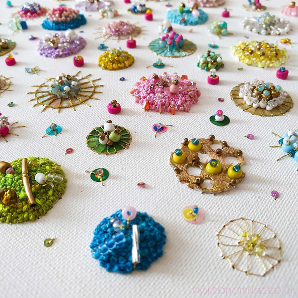 Close-up of colorful hand-embroidered canvas with beads, sequins, and gold leaf in circular patterns.
