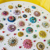 Circular mixed-media artwork featuring colorful beads, sequins, and embroidery on white canvas background.