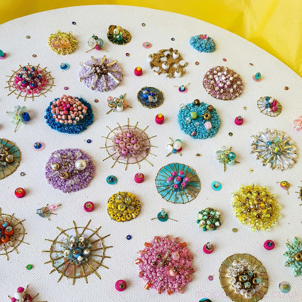 Circular mixed-media artwork featuring colorful beads, sequins, and embroidery on white canvas background.