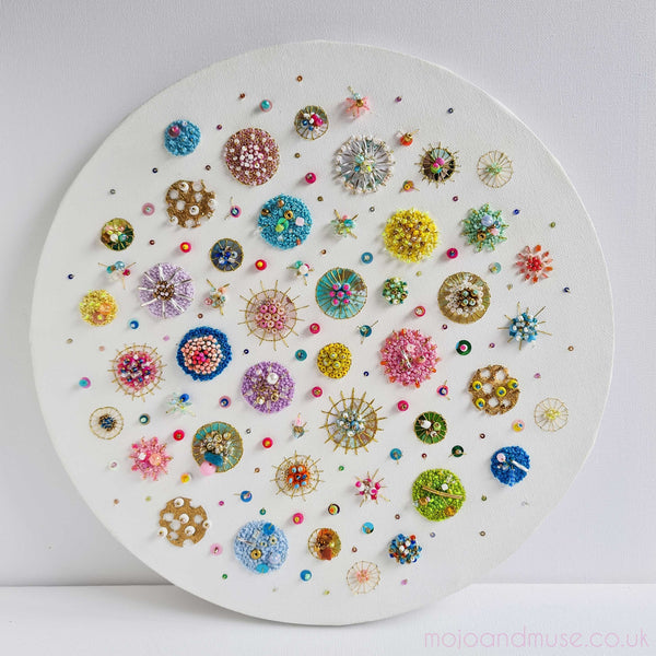 Circular canvas artwork with colorful embroidered beads, sequins, and gold leaf in intricate patterns titled Sea Jewels in the Snow.