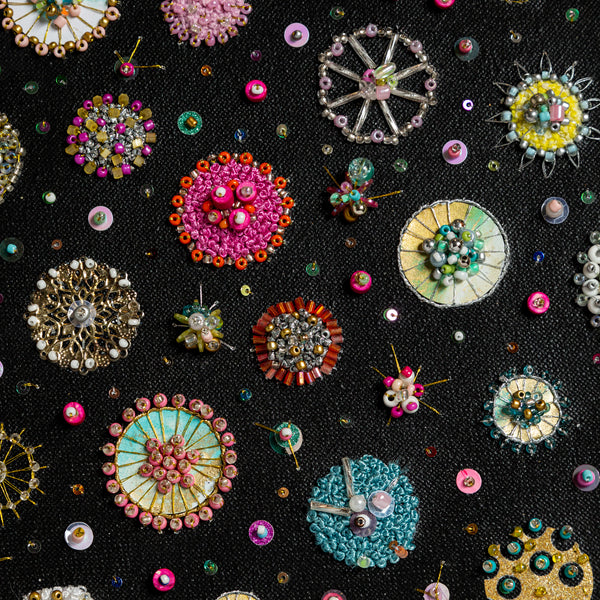 Close-up of intricate hand-embroidered sea jewels with beads, sequins, and gold foil on black canvas artwork.