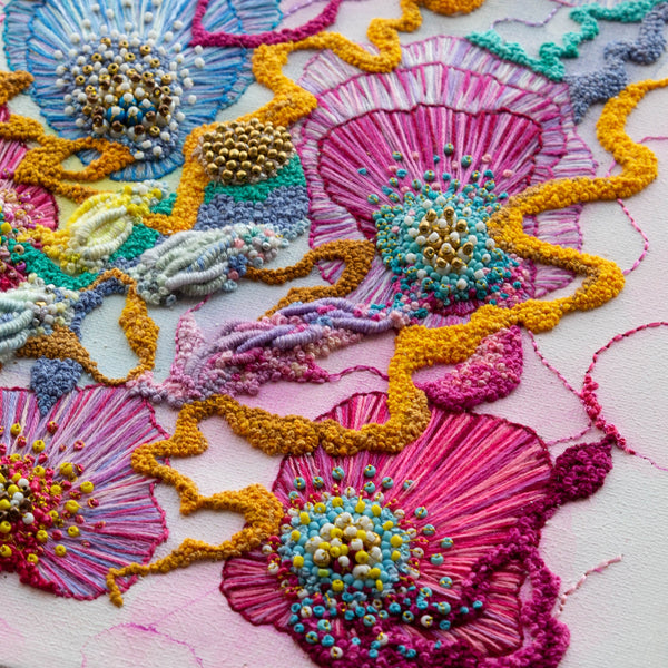 Close-up of vibrant floral embroidery with seed beads and gold thread on canvas in abstract nature design